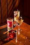 Fyra cocktails i olika glas står på ett träbord i varmt ljus.