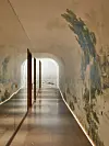 Lång gångtunnel med böjt tak, spegelvägg, väggmålning och ljus öppning mot vatten.