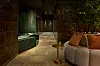Modern spa- och loungemiljö med kakelväggar, bänkar och soffa med kuddar i dämpad belysning.